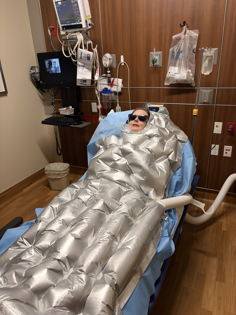 Leslie in hospital during a procedure, covered in an air warming blanket and wearing sunglasses