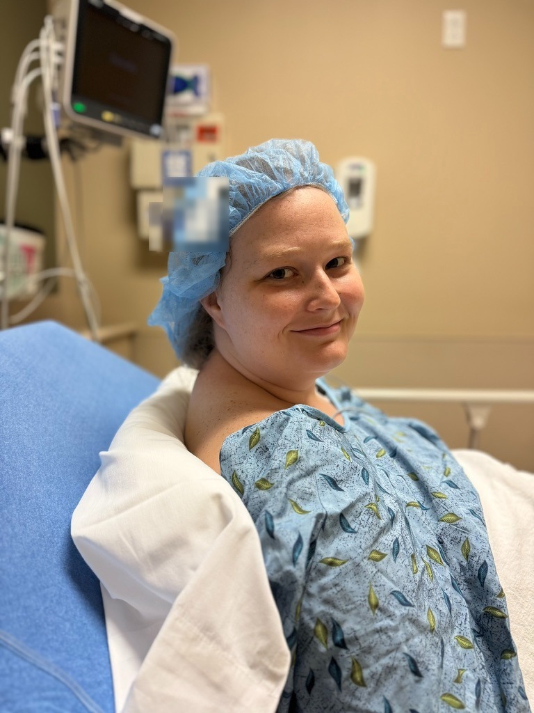 Leslie before a procedure, smiling in a hospital gown and blue surgical cap