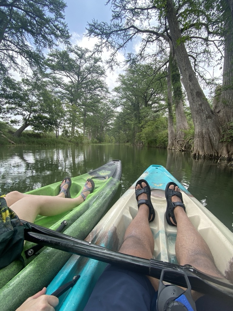 Surya and Leslie kayaking side by side down a cypress-lined Texas river